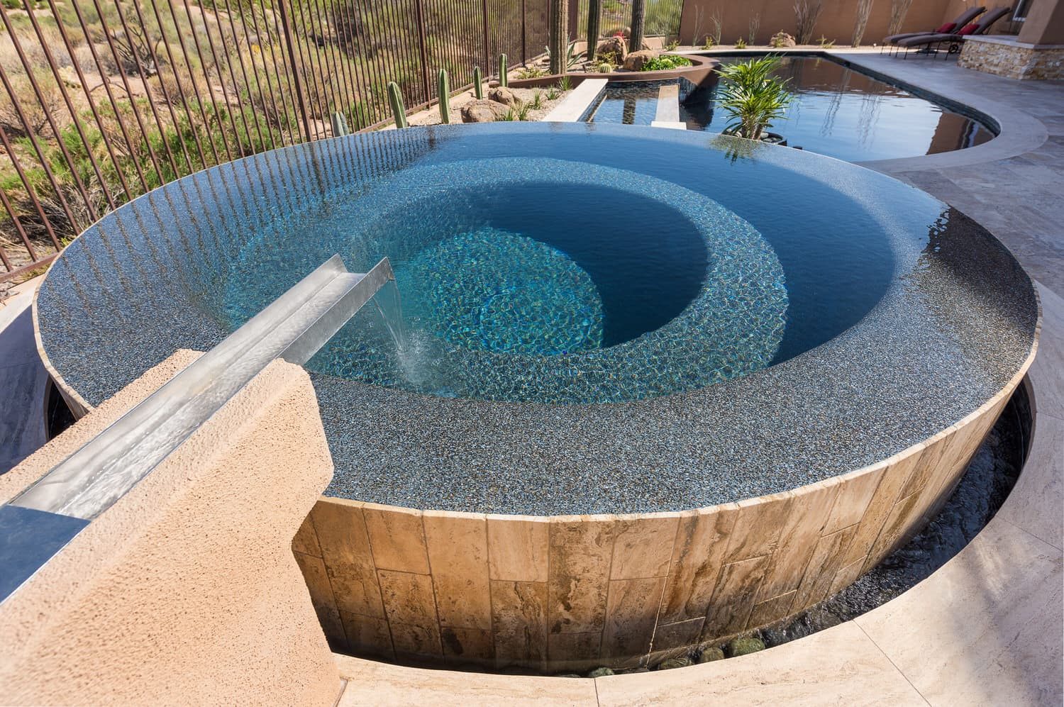 Raised spa spilling into a desert pool at sunset